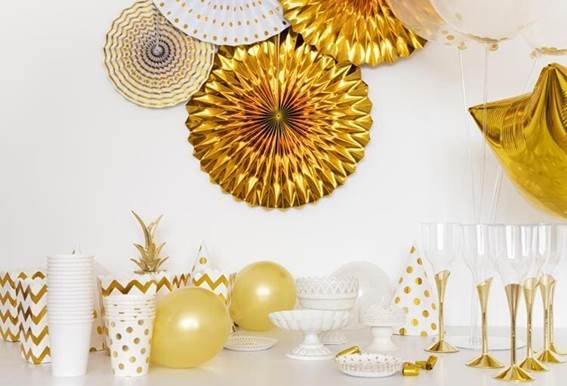 Nesta Imagem, é uma decoração de Réveillon, Festas Inesquecíveis, por que comemoramos todos os anos, aqui tem balões dourados, artigos de decoração branco e deourado sobre a mesa, na parede uma linda decoração simples e bonita.