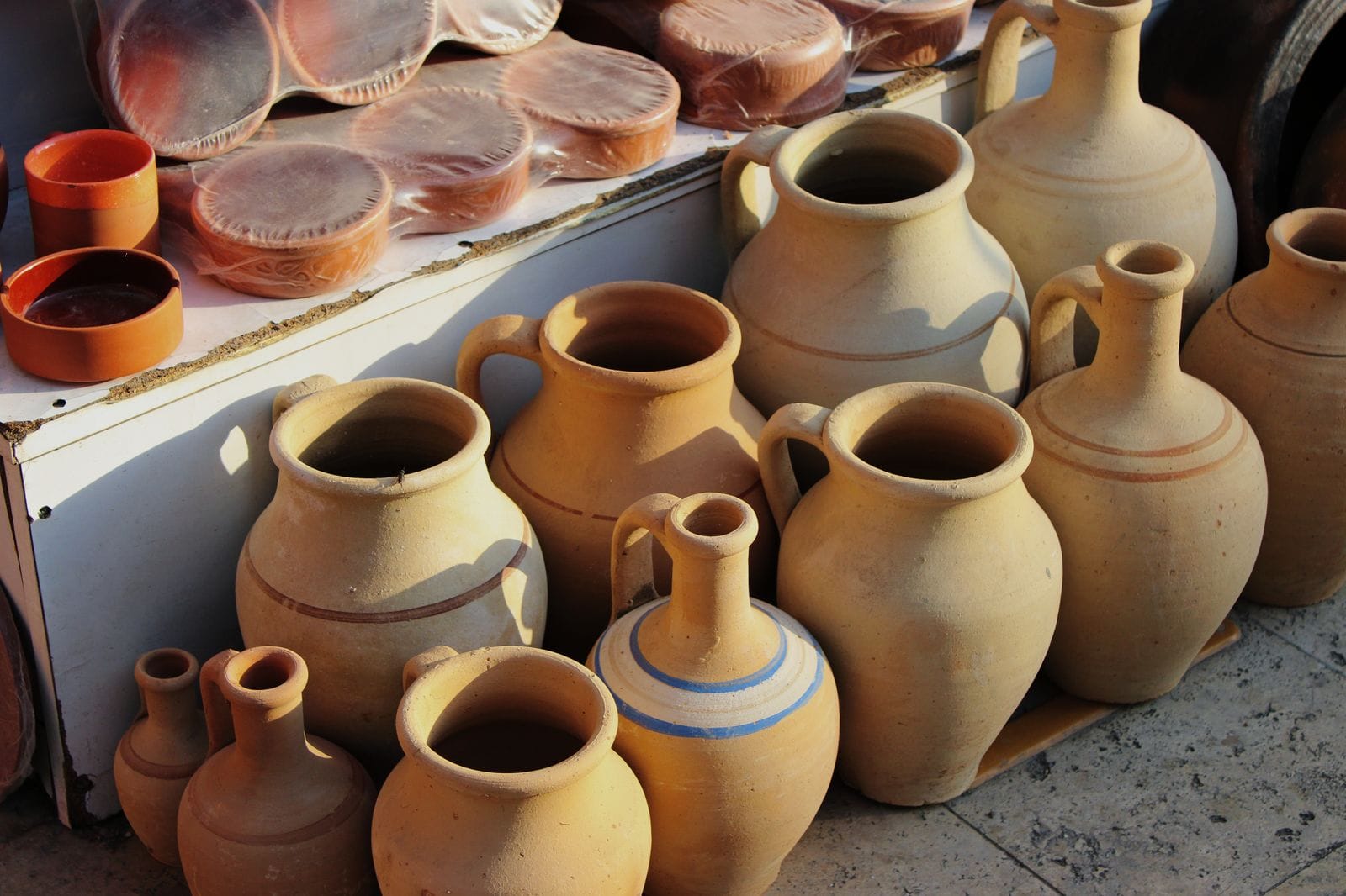 Vasos e jarras de cerâmica artesanal rústica em barro, tons terrosos, expostos em uma banca de feira
