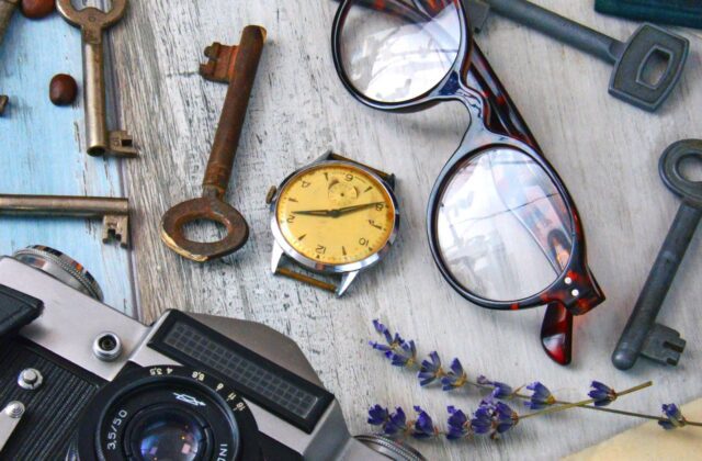 Still life de objetos vintage domésticos: câmera fotográfica antiga, chaves, óculos, relógio de pulso e cartas antigas sobre uma mesa