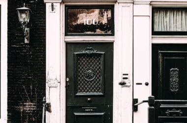 Fachada de uma casa antiga de tijolos com porta verde escura, janelas de guilhotina e vasos de plantas na entrada