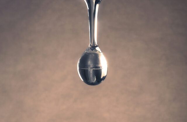 Close-up de uma gota de água se formando na ponta de uma torneira pingando