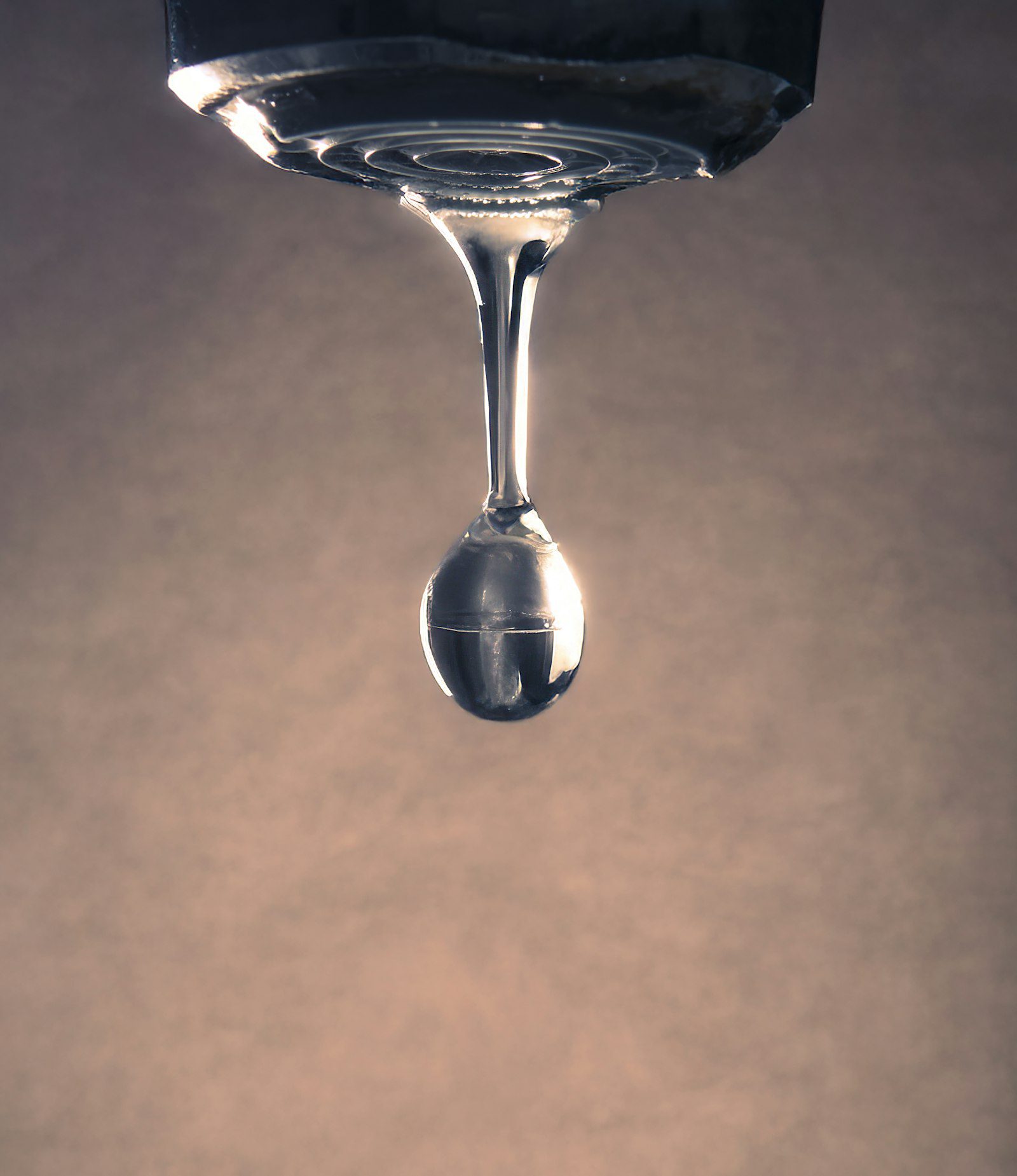 Close-up de uma gota de água se formando na ponta de uma torneira pingando